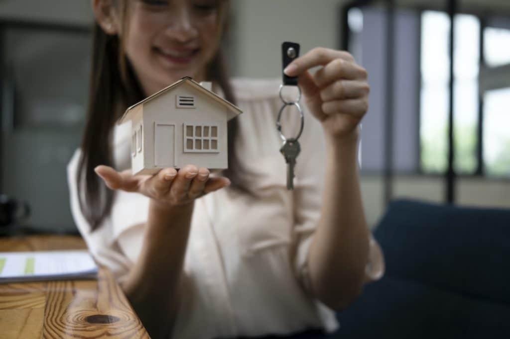 Young woman holding house model and key. Real estate and property concept.