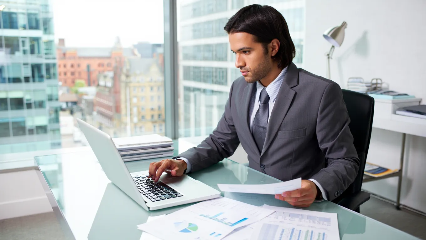 Property advisor analyzing investment reports and charts on laptop in modern Manchester office