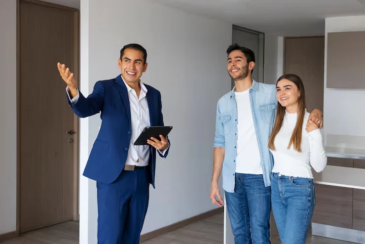 Property agent with tablet explaining features to young couple in modern unfurnished apartment
