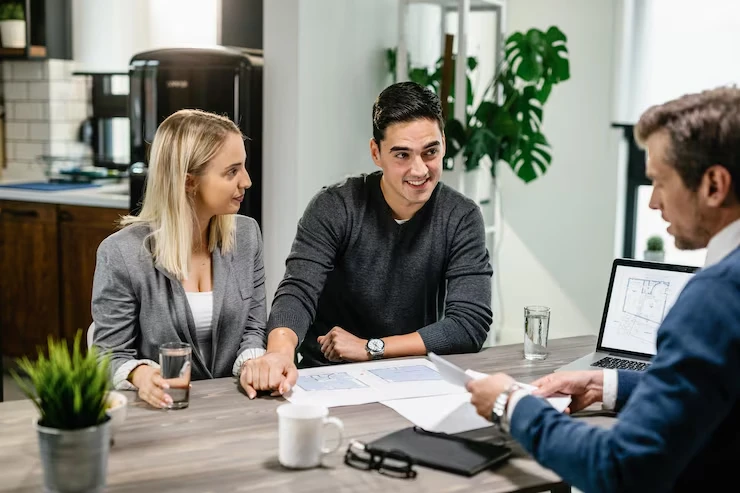 Property advisor showing laptop screen with floor plans to young couple at modern kitchen table
