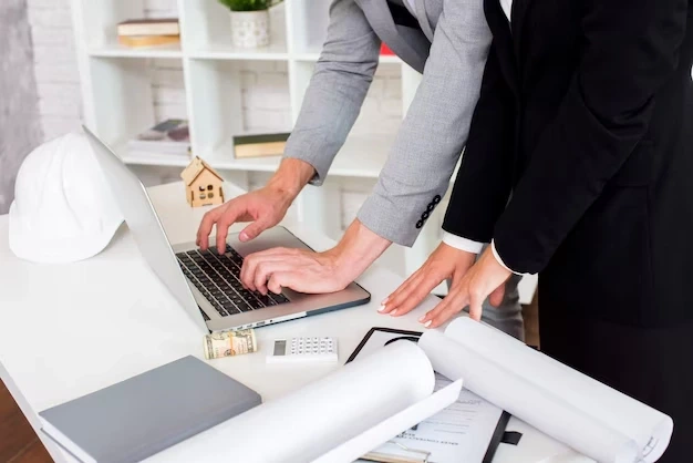 Advisors type on laptop next to house model and blueprints