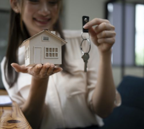 Young woman holding house model and key. Real estate and property concept.