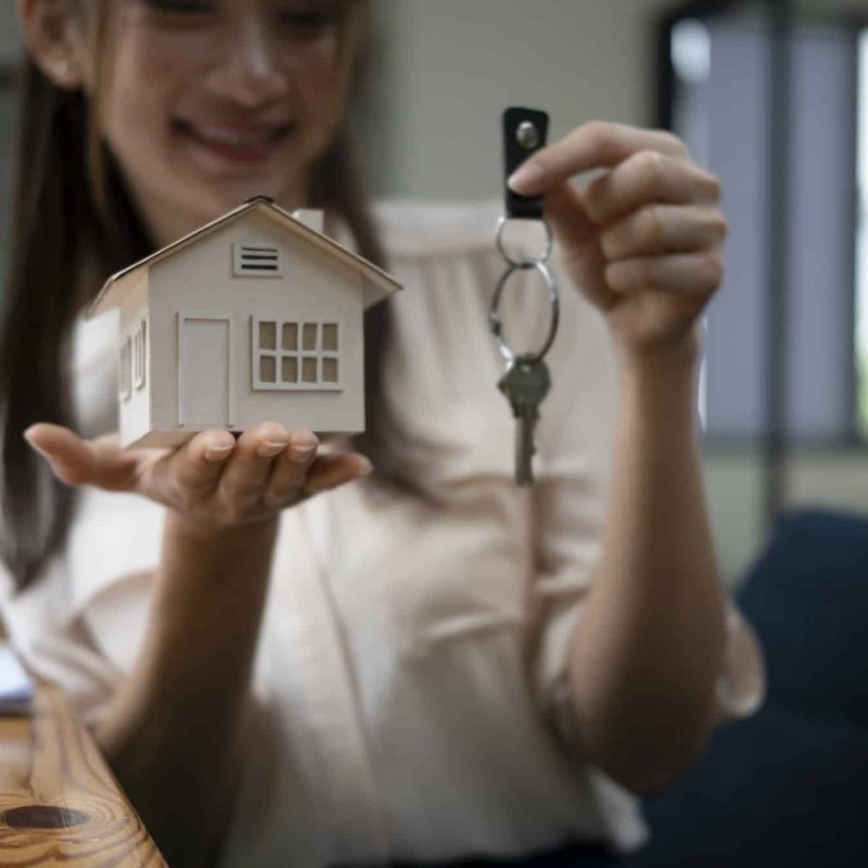 Young woman holding house model and key. Real estate and property concept.